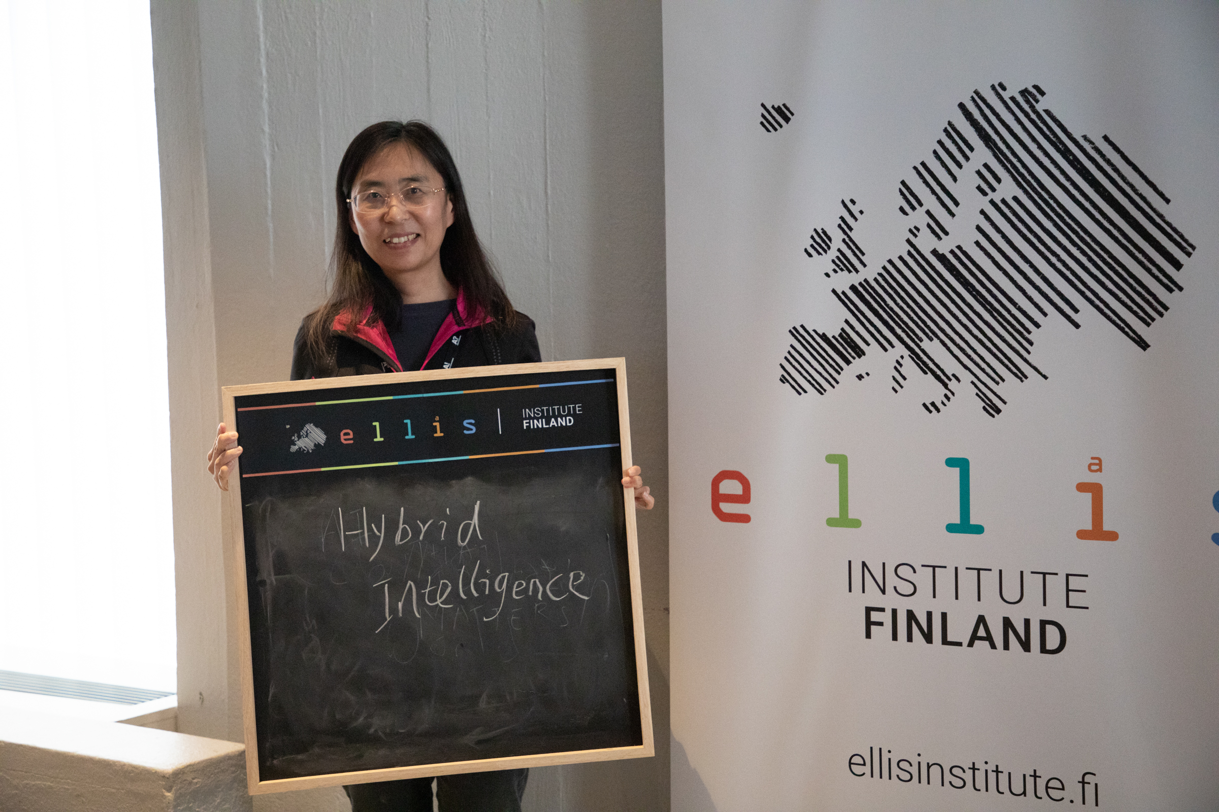 Woman standing in front of a banner holds a blackboard with text 'hybrid intelligence'