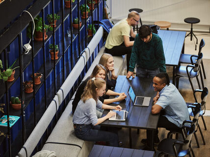 Group of people sitting and standing around table with laptops open