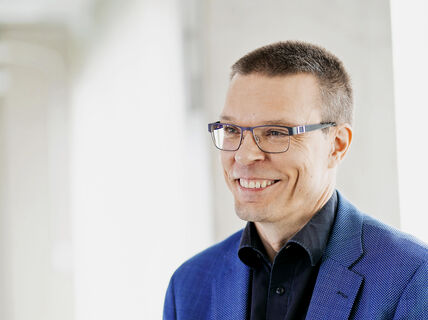 Smiling man with glasses and blue jacket looks off to the side