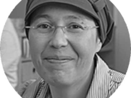 Portrait of a smiling woman with glasses and a hat.