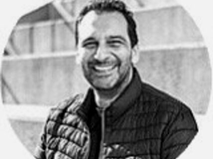 Portrait of a smiling, dark-haired man in a dark jacket.