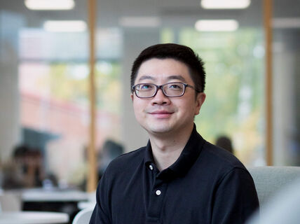 A person wearing a black long-sleeved shirt sits in a modern office space, with blurred office background.