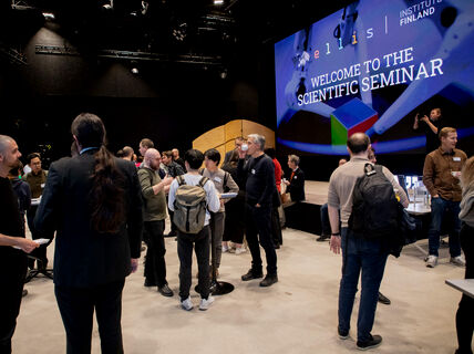 People mingling in front of a large stage and screen