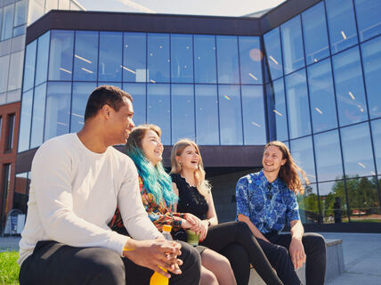 Four smiling people sitting outside in front of a building