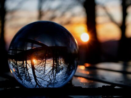 Clear glass ball on table reflects sun and bare trees in background
