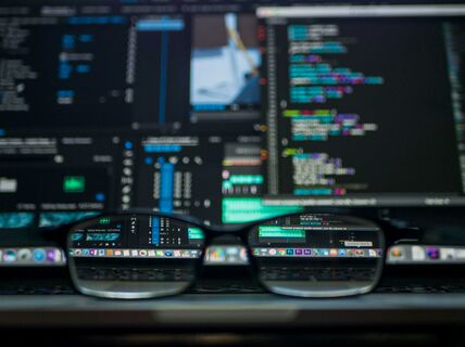 Black glasses on a laptop, reflecting a screen full of colourful code and data panels