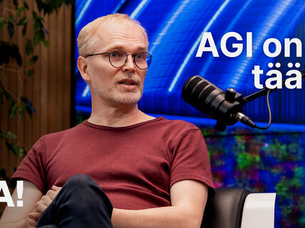 Man in glasses speaking into studio microphone, neon blue background with text: AGI on jo täällä