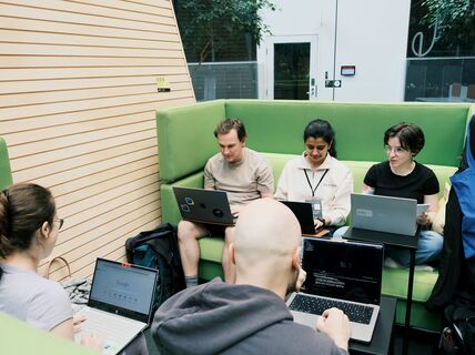 People sitting on green couches and working on laptops