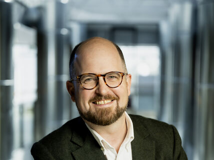 Smiling man wearing glasses against a blurred background of glass walls