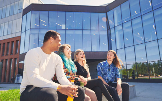 Four smiling people sitting outside in front of a building