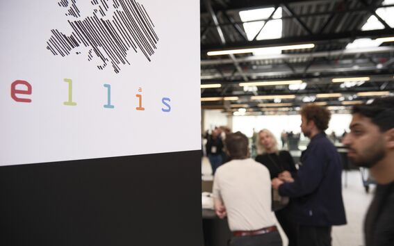 Sign with striped Europe map and colourful “ellis” logo beside people talking in a bright hall