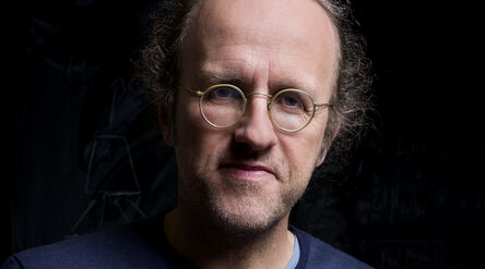 Person wearing round spectacles against a black background
