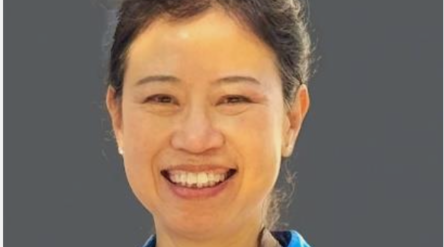 Smiling person wearing a blue shirt against a grey background
