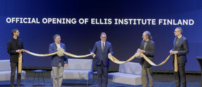 Five people holding a cut gold ribbon with text in background: OFFICIAL OPENING OF ELLIS INSTITUTE FINLAND