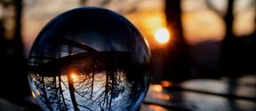 Clear glass ball on table reflects sun and bare trees in background