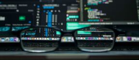 Black glasses on a laptop, reflecting a screen full of colourful code and data panels