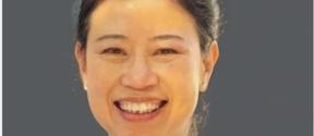 Smiling person wearing a blue shirt against a grey background