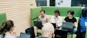 People sitting on green couches and working on laptops