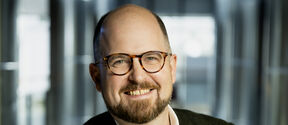 Smiling man wearing glasses against a blurred background of glass walls