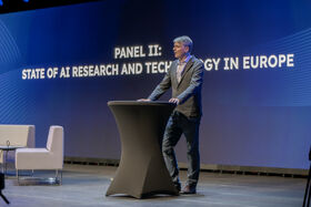 Neil Lawrence standing at a podium speaking with text in background: State of AI research and technology in Europe