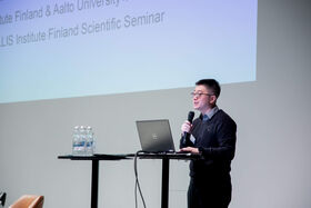 Man standing at podium with laptop, holding a microphone