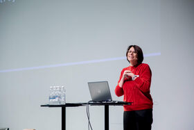 Women in a red sweater standing at a podium with a laptop