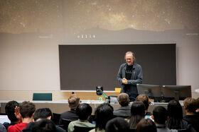 Person standing in front of a blackboard giving a lecture to an audience