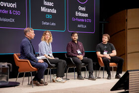 Four people sitting in chairs on a stage in front of a large screen.