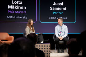 Two people sitting on a stage in front of a screen.
