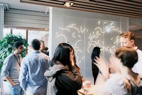 People standing talking, with a white wall with world map in background