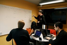 People with laptops in a small conference room looking at a whiteboard