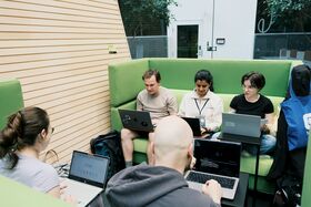 People sitting on green couches and working on laptops