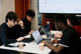 People working on laptops, seated around a table.