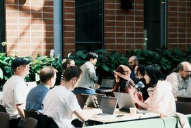 People sitting at tables with laptops, in an atrium with a brick background
