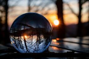 Clear glass ball on table reflects sun and bare trees in background