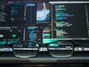 Black glasses on a laptop, reflecting a screen full of colourful code and data panels