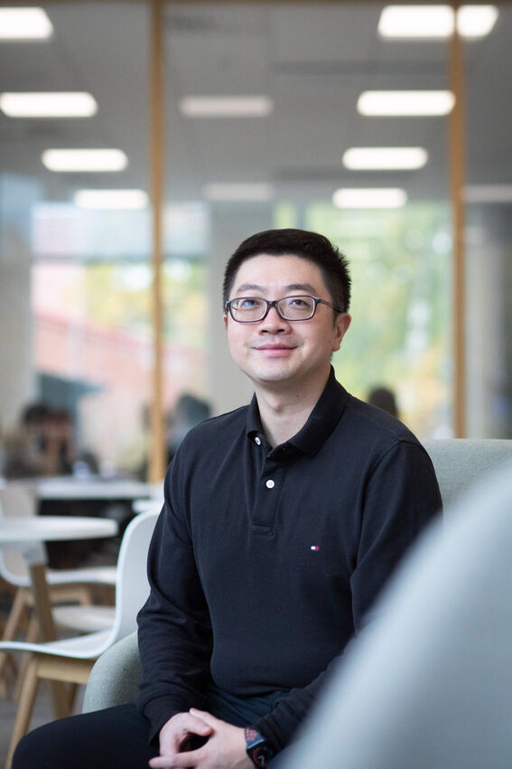 A person wearing a black long-sleeved shirt sits in a modern office space, with blurred office background.