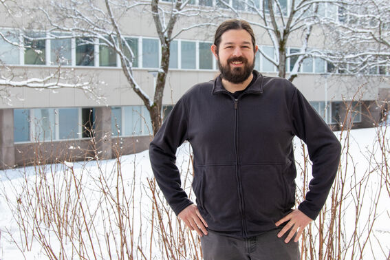 Person in dark jacket stands in snowy yard before office building with bare, snow-covered trees