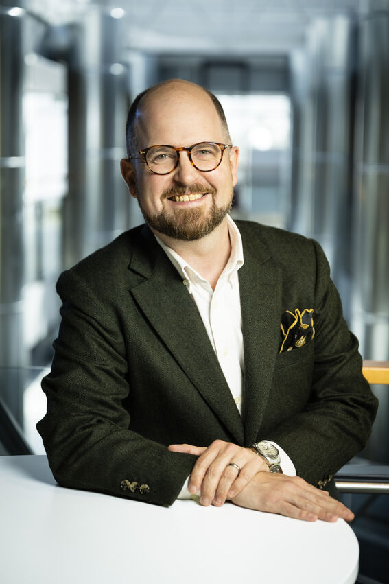Smiling man wearing glasses against a blurred background of glass walls