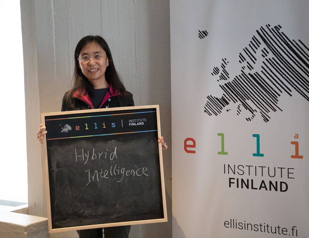 Woman standing in front of a banner holds a blackboard with text 'hybrid intelligence'